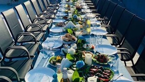 A long dining table set outdoors with chairs on both sides, surrounded by a scenic view of hills and buildings. - Hotel Villa Lapa (Telavi)
