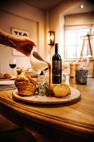 A hand pouring sauce over a dish on a wooden table, with a bottle of wine and a sign reading "TEA" in the background.