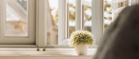 A window with white blinds, a small potted plant on the sill, and a glimpse of a building outside.