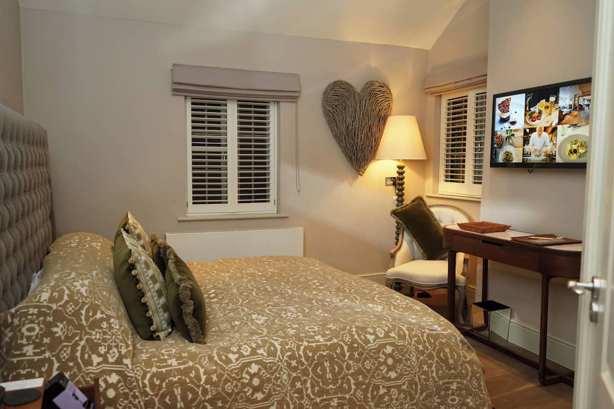 A bedroom with a patterned bedspread, a heart-shaped wall decoration, a desk with a lamp, and a television displaying a collage of images.