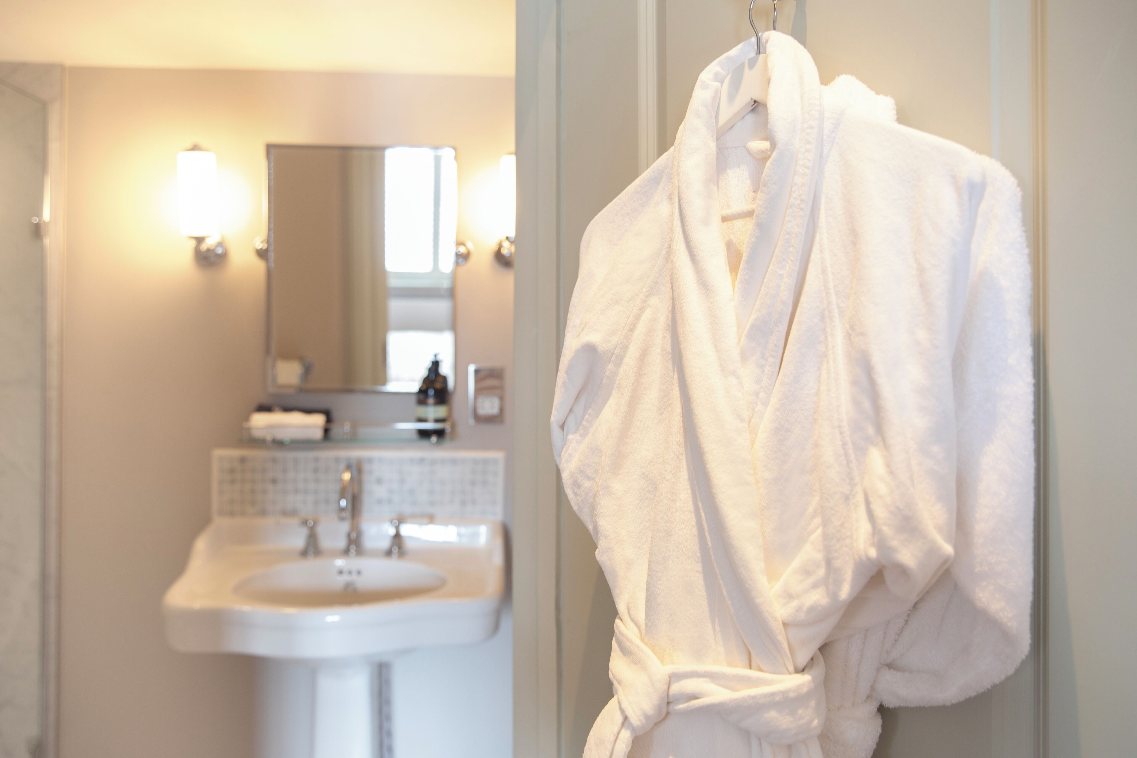 A bathroom with a sink, mirror, and a white robe hanging on a door.
