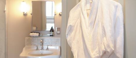 A bathroom with a sink, mirror, and a white robe hanging on a door.