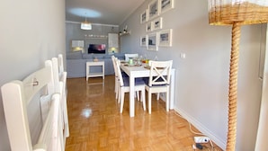 Um espaço de estar moderno com área de jantar, cozinha e TV ao fundo.