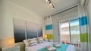 Um quarto com cama, mesa de cabeceira, janela com cortinas e vista para o exterior.