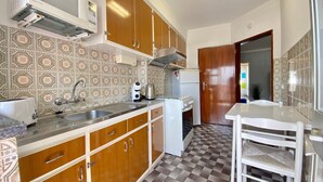Uma cozinha compacta com armários de madeira, bancada branca, pia, fogão e geladeira.