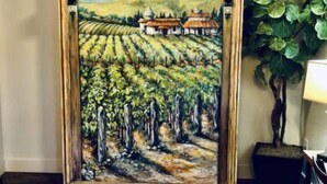 Ein gerahmtes Gemälde von einem Weinberg mit Gebäuden im Hintergrund.