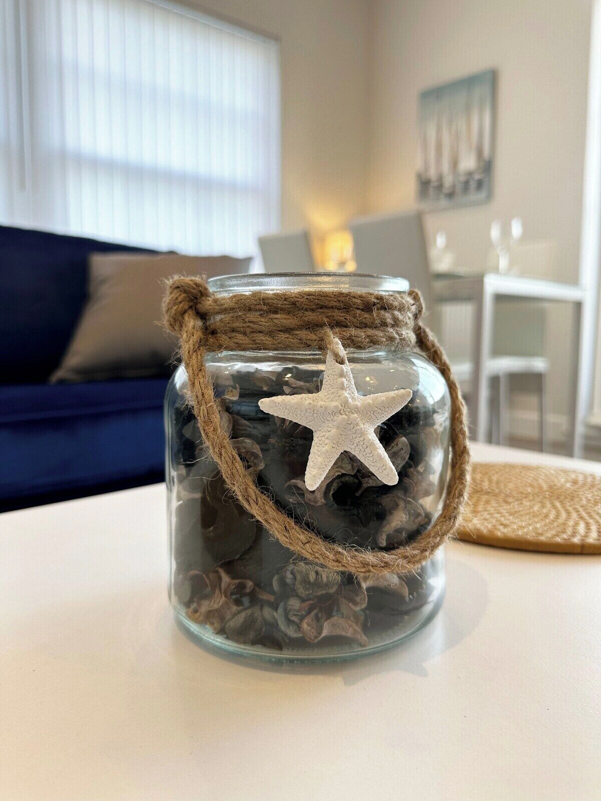 Un bocal en verre décoré d’une étoile de mer, rempli de pierres, posé sur une table.