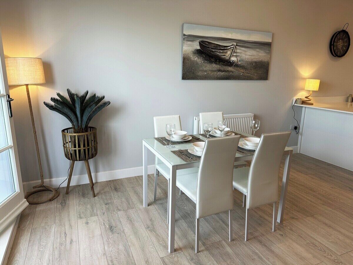 A dining area with a white table set for four, a potted plant, and a painting of a boat on the wall.