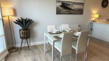 A dining area with a white table set for four, a potted plant, and a painting of a boat on the wall.