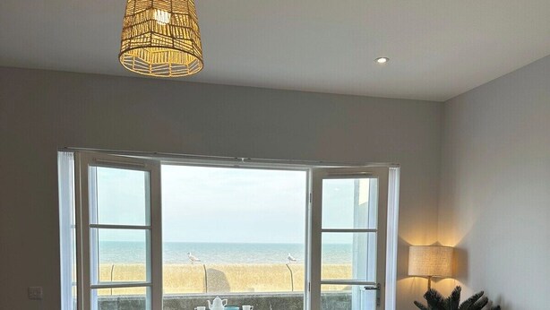Uma área de refeições com vista para a praia, uma mesa posta com pratos e copos, e um lustre pendurado.