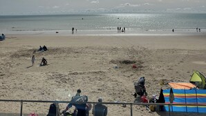 Uma praia com pessoas, céu claro e um litoral distante.