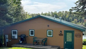 A cabin with a green door, two windows, a porch with chairs, a grill, and a sign reading "Parker's Cabin." - Cozy Cabin on Rangeley Lake  (Rangeley)