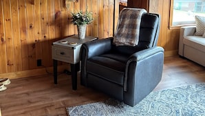 A cozy cabin interior with wooden walls, a leather chair, a small table with a plant, and a window with a view. - Cozy Cabin on Rangeley Lake  (Rangeley)