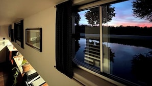 A room with a large window overlooking a body of water and a sunset. - Au fil de Leau (Plobsheim)