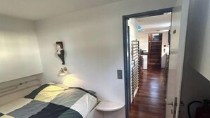 A bedroom with a bed, a bedside table, a wall-mounted shelf, and a door leading to a hallway. - Au fil de Leau (Plobsheim)