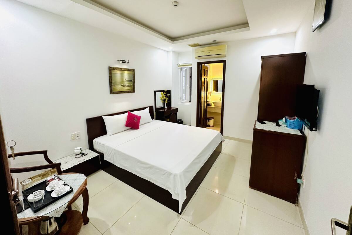 Habitación de hotel con cama, mesita de noche, silla y un pequeño comedor con una bandeja de platos.