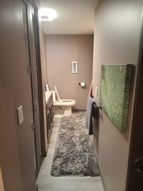 A narrow hallway leading to a bathroom with a toilet, a sink, and a towel rack.