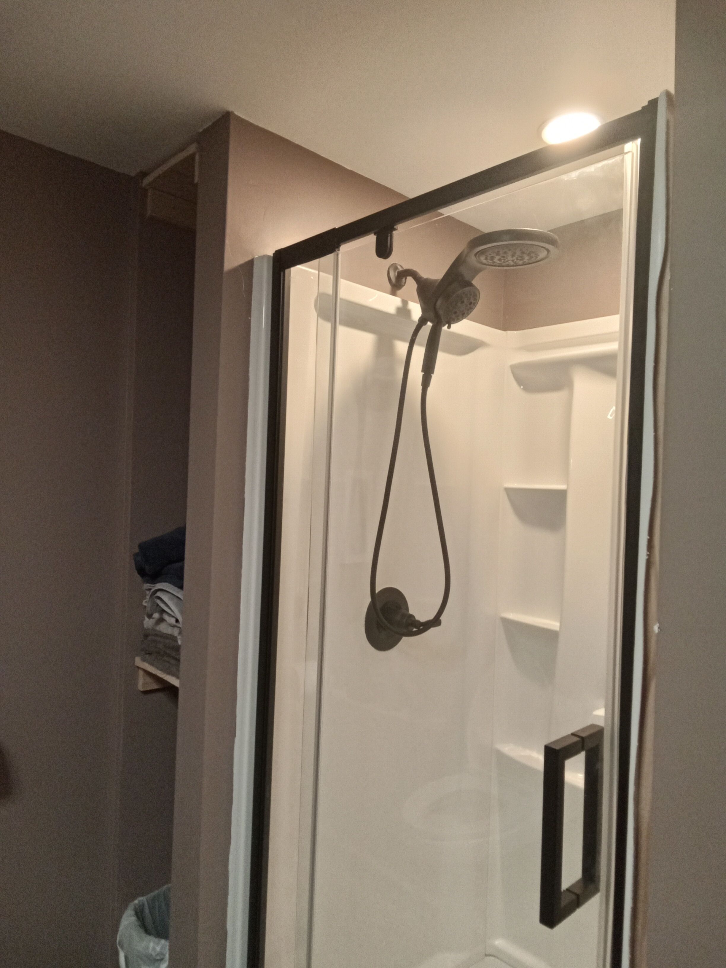 Une douche fermée par des parois en verre, dotée d’un pommeau de douche à main, d’un porte-serviettes et d’une étagère.