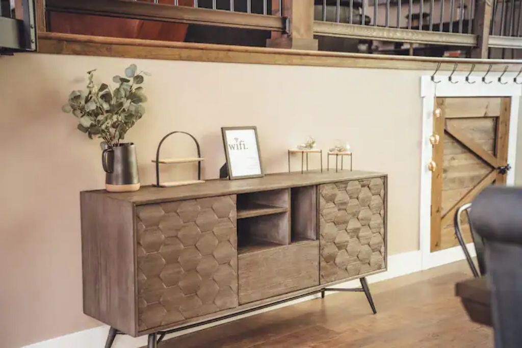 Une console en bois ornée de motifs hexagonaux, un vase avec des feuilles vertes, un tableau encadré et une petite table sur laquelle est posé un vase.