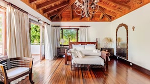 A spacious bedroom with a wooden ceiling, a large bed, a chair, and a nightstand with a lamp.