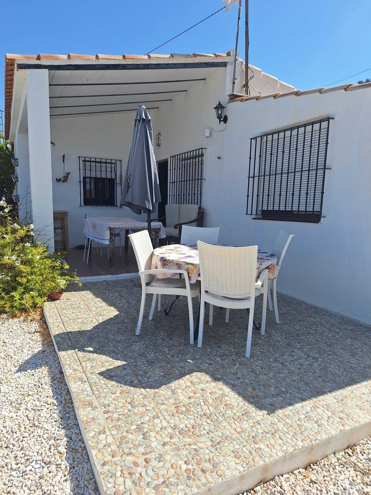 Un patio couvert avec une table et des chaises, un fauteuil suspendu et un petit coin jardin.