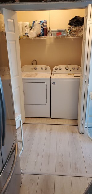 Ein Waschraum mit zwei Whirlpool Waschmaschinen und Trocknern, einem Holzboden und einem Regal über den Trocknern mit verschiedenen Gegenständen.