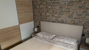 A bedroom with a stone wall, a wooden panel, a bed with floral bedding, and a nightstand with a lamp.