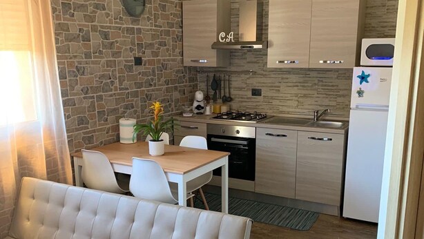 A modern kitchen with a stone wall, a dining table with chairs, and a sofa in a living area.