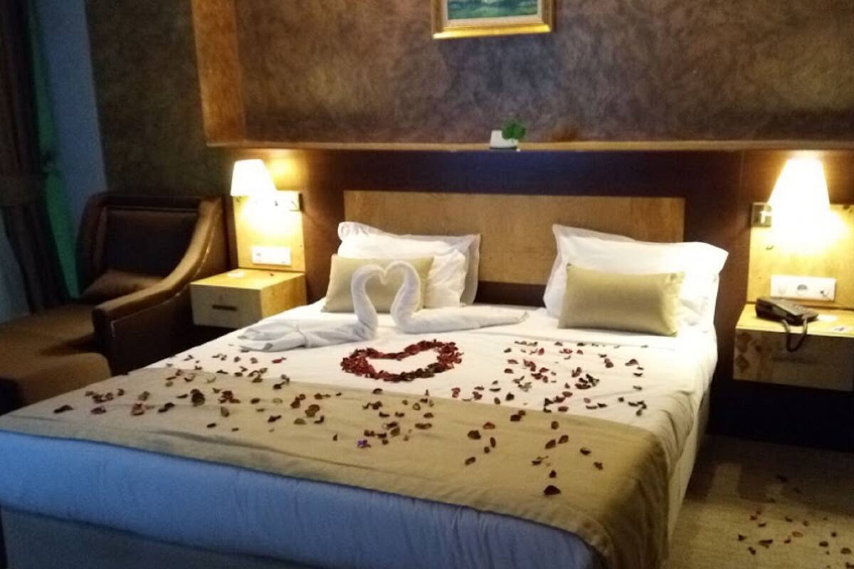 Una habitación de hotel con cama, dos mesitas de noche, una silla y una estantería en la pared.