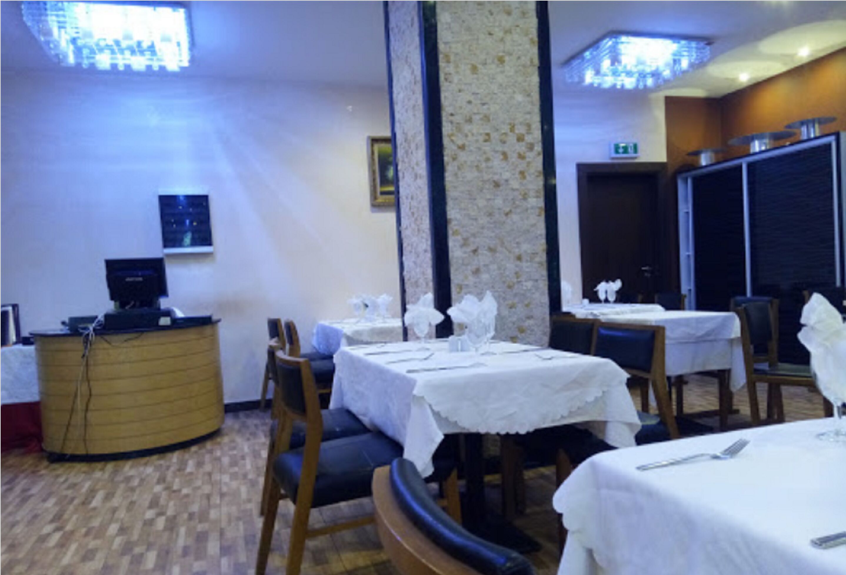 A restaurant with tables set for dining, a reception desk, and a patterned column.