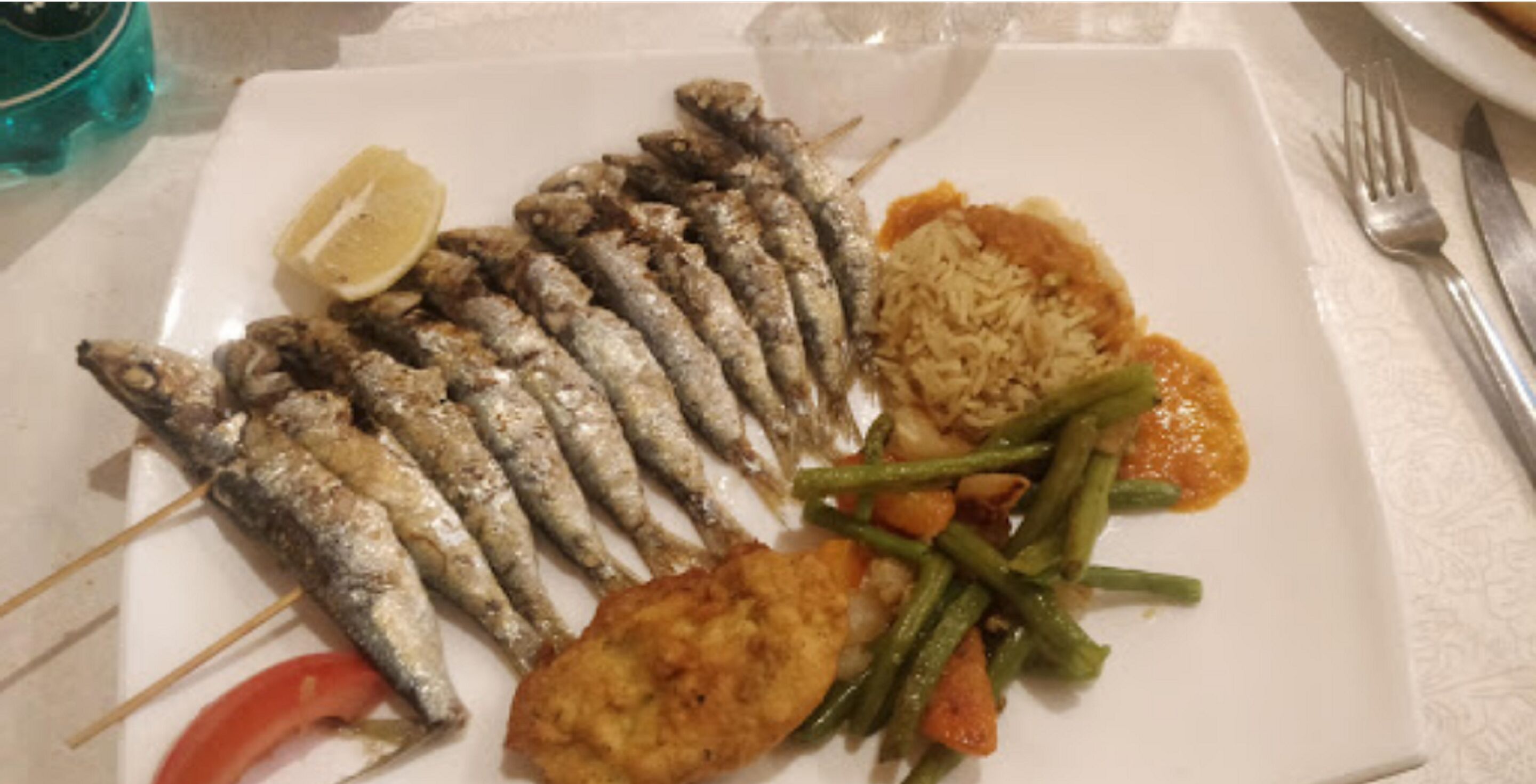 Un piatto con pesce alla griglia, riso, fagiolini e spicchio di limone.
