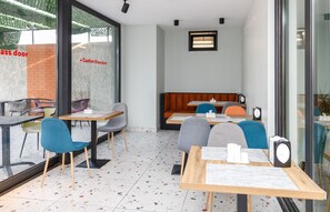 A modern cafe with tables and chairs, a glass door with a caution sign, and a brick wall in the background.