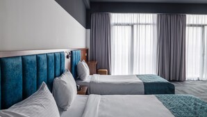 Une chambre d’hôtel avec deux lits, une t ête de lit en bois, une petite table et une vue sur l’extérieur grâce à de grandes fenêtres.