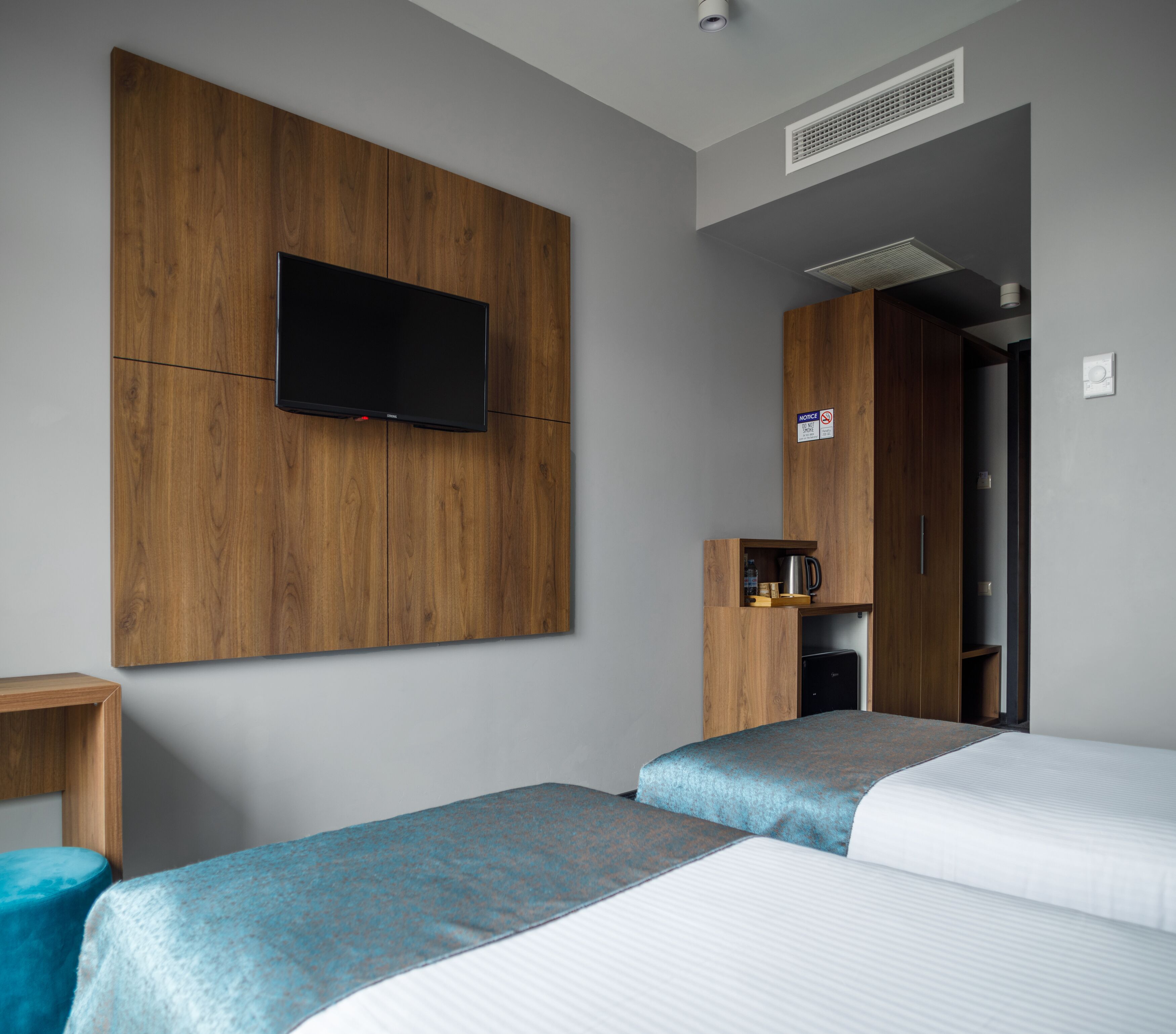 A hotel room with two beds, a TV mounted on a wooden panel, a coffee machine, and a small cabinet.
