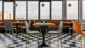 Un restaurant moderne avec un sol à carreaux, des banquettes et des tables. De grandes fenêtres offrent une vue sur la ville.