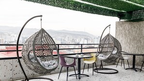 Un balcon avec deux fauteuils suspendus, une table et des chaises, offrant une vue sur la ville.