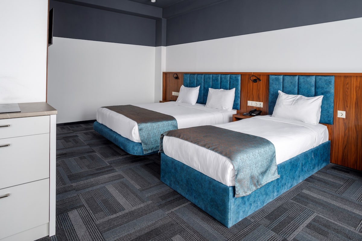 Quarto de hotel com duas camas, uma escrivaninha e um guarda-roupa.