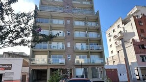 Un edificio de varios pisos con balcones, un coche aparcado y una fachada visible.