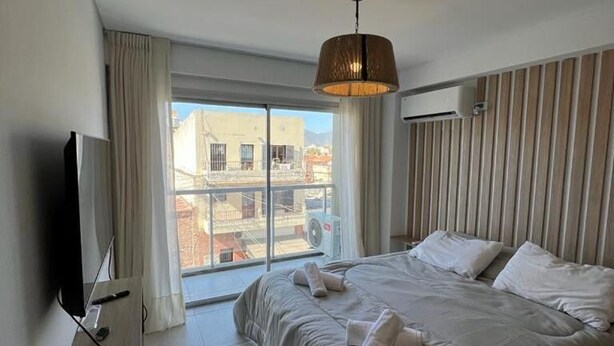 Habitación de hotel con una cama grande, televisión, ventana con cortinas y vistas a edificios.