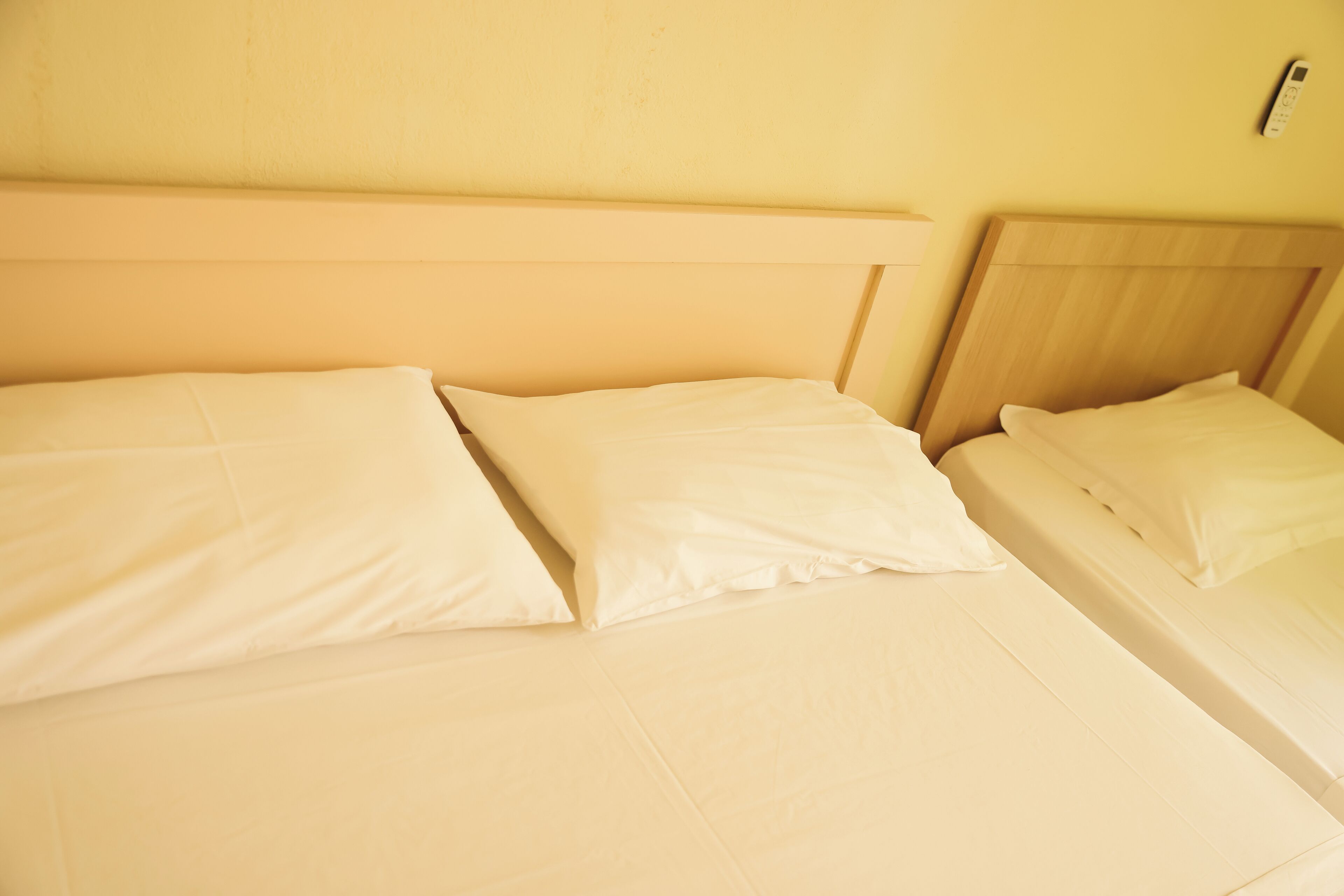 Dos camas con sábanas blancas y cabeceros de madera en una habitación con paredes amarillas.