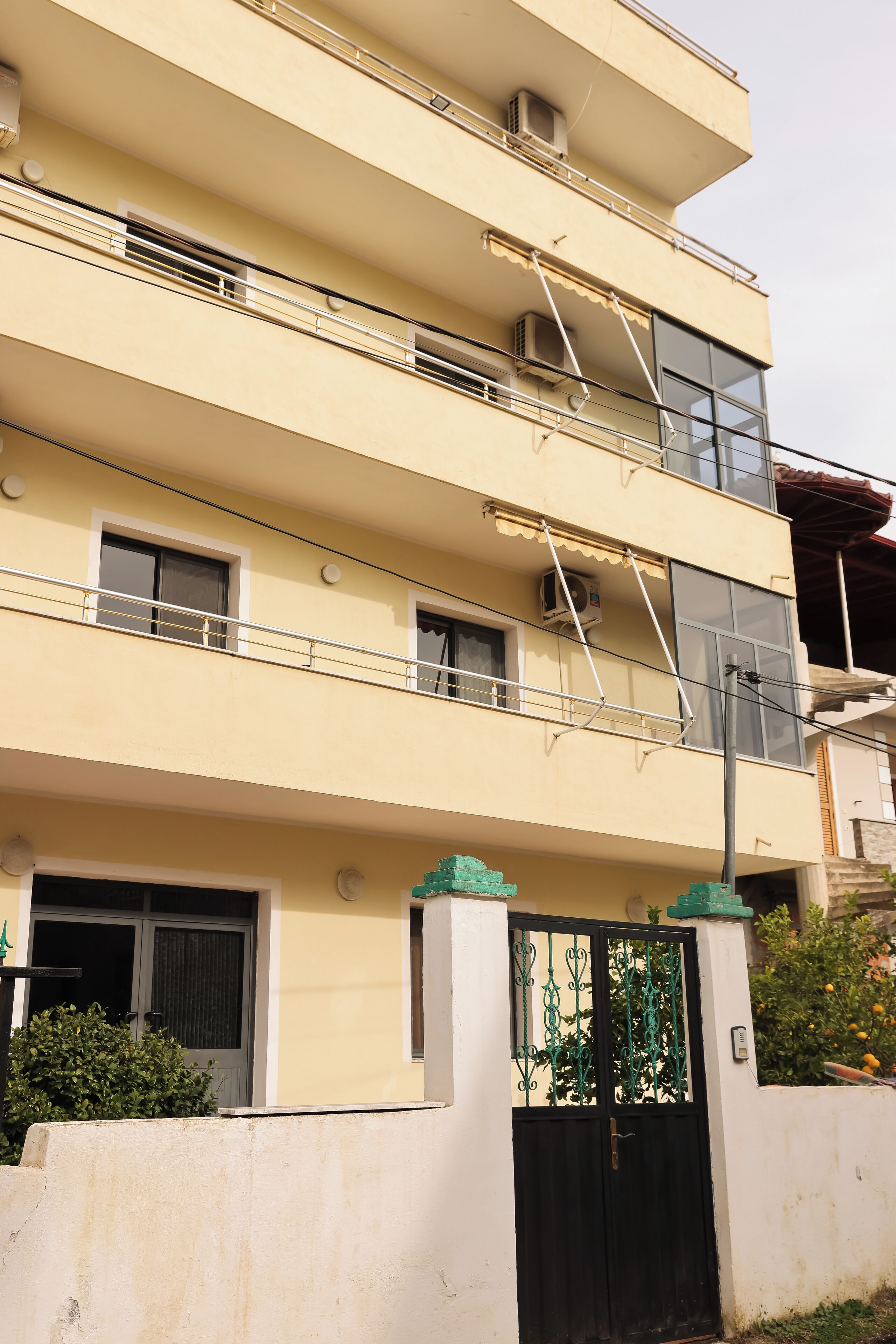Un edificio de varios pisos con balcones, unidades de aire acondicionado y una entrada protegida por una puerta.