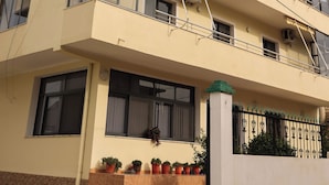 A multi-story building with balconies, large windows, and potted plants on the ground floor.