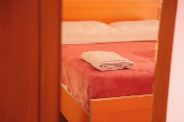 A bed with a red bedspread and a folded white towel. - Haka guesthouse (Golem)