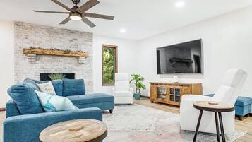 A modern living room with a blue sofa, white armchairs, a wooden coffee table, and a fireplace.