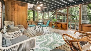 A covered wooden deck with wicker furniture, a table, and chairs.