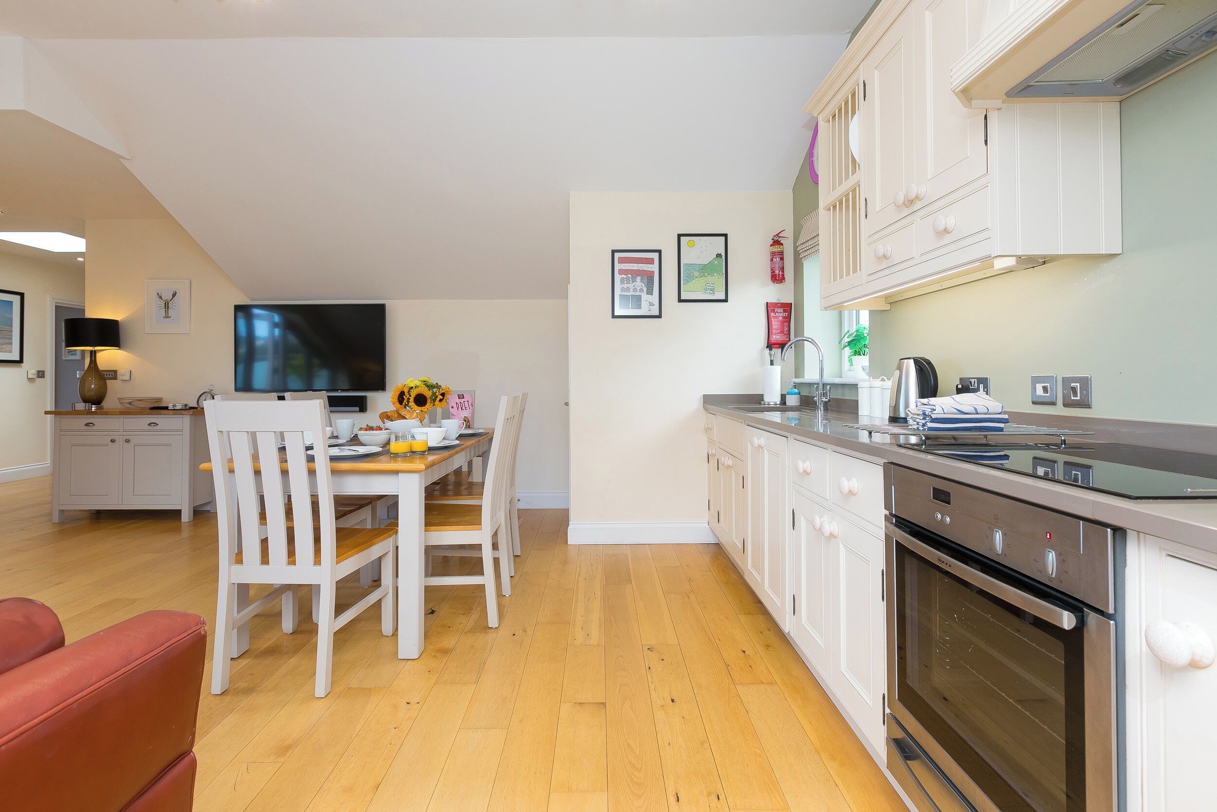 Una cocina moderna con armarios blancos, horno integrado y un comedor con mesa y sillas de madera.