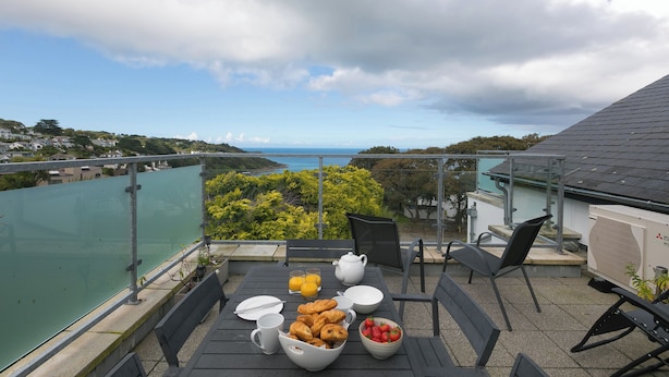 Un balcon avec une table préparée pour le petit-déjeuner, offrant une vue panoramique sur la mer et les collines.