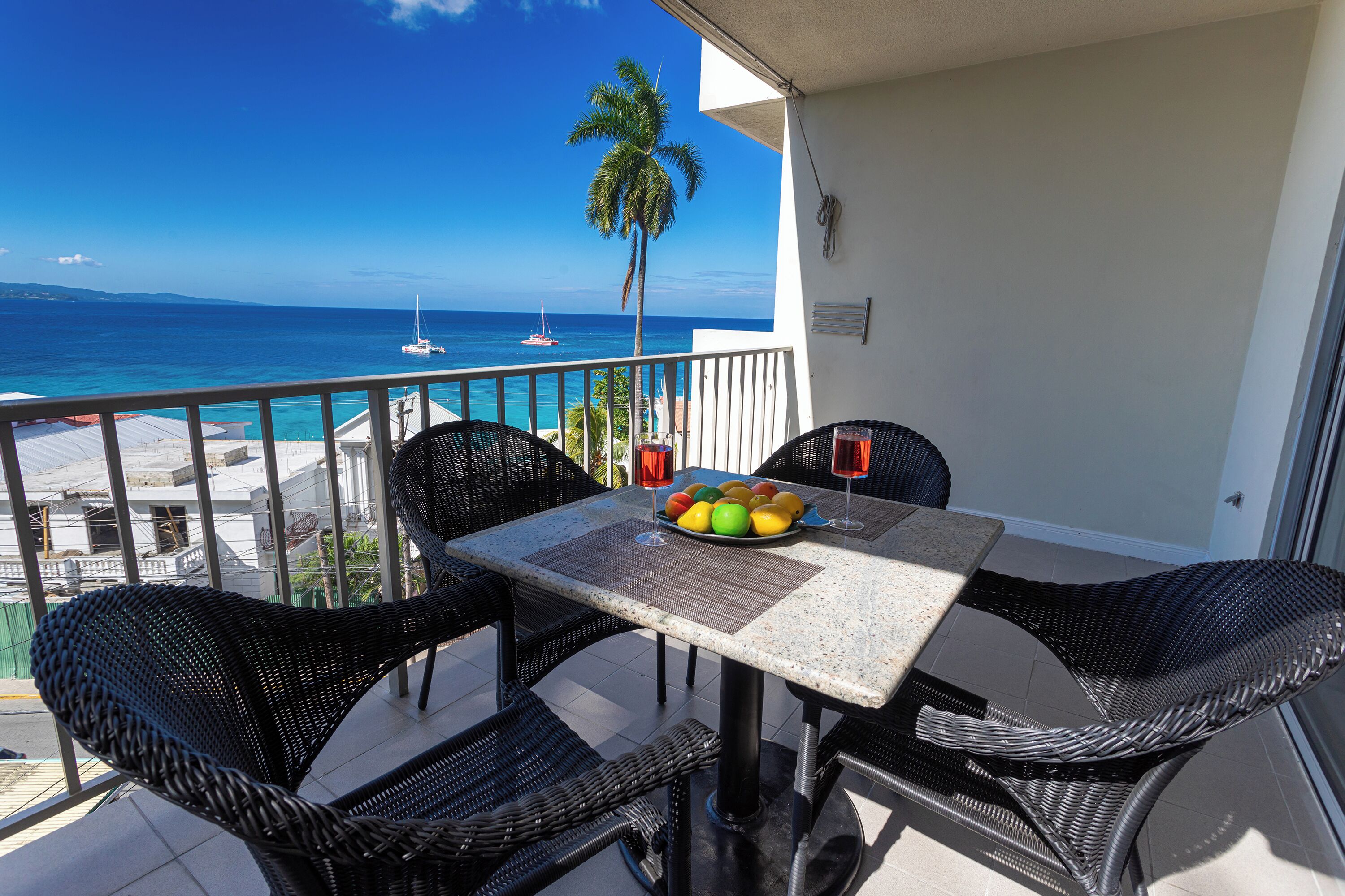 Un balcon avec une table et des chaises, une vue sur l’océan et un palmier.
