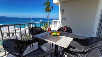 Un balcon avec une table et des chaises, une vue sur l’océan et un palmier.