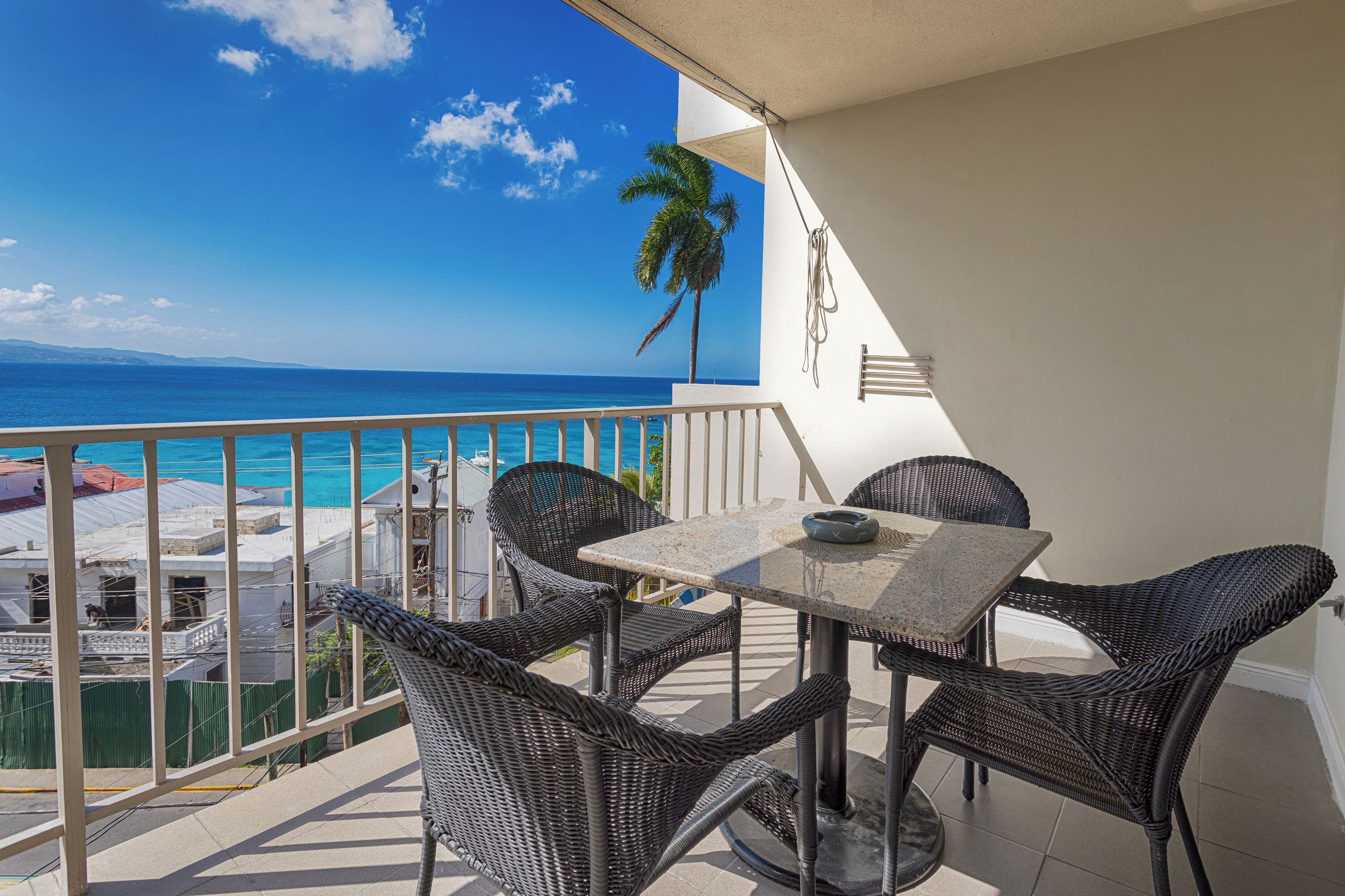 A balcony with wicker furniture, a view of the ocean, and a palm tree.